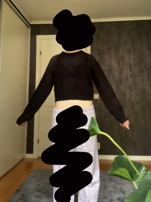 Svart stickad cropped tröja - Snygg svart stickad tröja med hålmönster och croppad passform. Tröjan har långa ärmar, rund halsringning och ribbade muddar vid ärmslut och nederkant. Perfekt att styla över ett linne eller t-shirt för en trendig look.