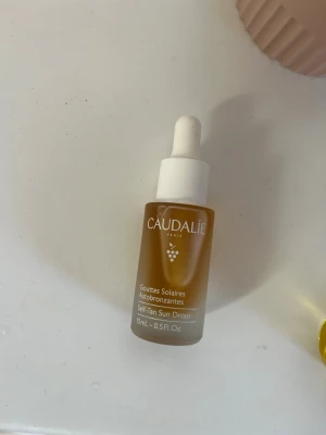 Caudalie Self-Tan Sun Drops 15ml - Caudalie Self-Tan Sun Drops är brun-utan-sol-droppar i en frostad glasflaska med pipett. Produkten är ljusbrun och används för att ge huden en solkysst ton. Flaskan rymmer 15 ml och har en vit pipettkork för enkel dosering.
