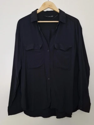 Svart skjorta med fickor - Stilren svart skjorta från Zara.  Skjortan har två stora bröstfickor med lock, klassisk krage och knäppning framtill. Tillverkad i mjukt material som ger ett avslappnat intryck. Perfekt att styla lager på lager. Storlek XXL, från viskos. Fint skick