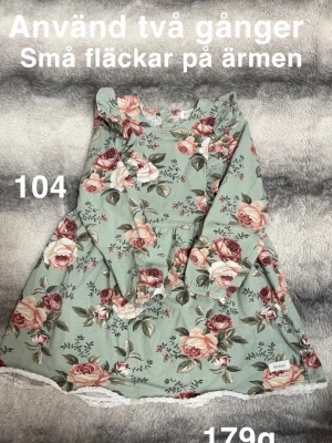 Blommig långärmad klänning - Supersöt långärmad klänning från newbie i grönt med stort blommönster i rosa, vinrött och beige. Klänningen har volang vid axlarna och spetskant nertill. Perfekt för dig som gillar romantisk stil!🌸Använd två gånger. Små fläckar på ärmen. Storlek 104