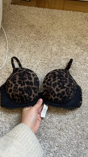 Leopardmönstrad push-up bh med spets - Snygg push-up bh med leopardmönster i brunt och svart. Bh:n har vadderade kupor, justerbara axelband och dekorativ svart spets längs nederkanten. Perfekt för dig som gillar djurmönstrat och vill ha lite extra lyft.