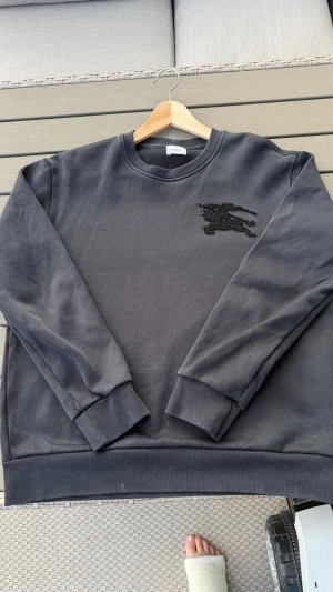Svart sweatshirt från Burberry - Cool svart sweatshirt från Burberry med klassisk rund hals och ribbade muddar. På bröstet finns Burberrys ikoniska broderade ryttare i svart. Perfekt oversized fit för en avslappnad stil.