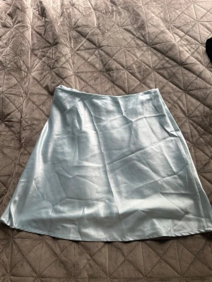 Ljusblå satin kjol från Chiquelle - Säljer en ljusblå, glansig satin kjol från Chiquelle. Kjolen har en enkel och stilren design med lätt utställd form och slät midja. Perfekt för dig som gillar en clean och trendig look.