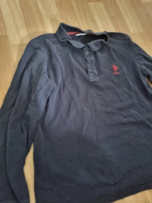 Ralph lauren - Svart långärmad skjorta från U.S. Polo Assn. med klassisk krage och knappar framtill. Diskret röd logotyp broderad på bröstet. 