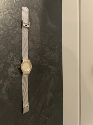 Stilren silverfärgad meshklocka - Minimalistisk klocka med mesharmband i silver och rund urtavla med gulddetaljer. Klockan har ett klassiskt spänne och en enkel, modern design som passar till många stilar. (Funkar ej!!, behöver nytt batteri.)