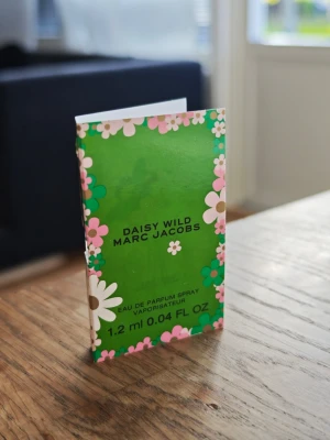 Daisy Wild parfymprov Marc Jacobs - Tagit 1 sprut. Daisy Wild från Marc Jacobs som parfymprov, 1,2 ml Eau de Parfum Spray. Kommer i en liten glasflaska med vit spraykork och grön kartong med blommigt mönster i rosa, vitt och grönt. Perfekt att ha med i väskan för en fräsch doftboost.