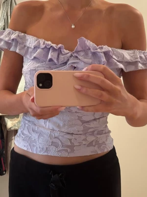 Ljuslila offshoulder topp med volang - Superfin ljuslila offshoulder topp med volangkant och blommigt mönster. 
