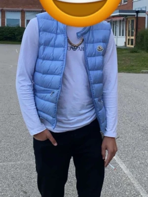 Ljusblå dunväst från Moncler - Ljusblå dunväst från Moncler med klassisk quiltad design och hög krage. Västen har två dragkedjeförsedda fickor framtill och riktigt snygg till streetwear. Pris kan väl diskuteras vid snabb affär 