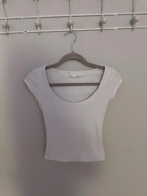 Vit croppad topp  - Säljer en enkel och snygg vit croppad topp. Toppen har korta ärmar, rundad urringning och är tillverkad i mjuk bomull. Perfekt till jeans eller kjol för en clean look.