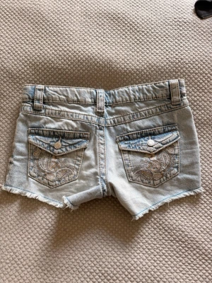 Ljusblå jeansshorts med broderi - Snygga ljusblå jeansshorts med slitna kanter och broderade detaljer på bakfickorna. Korta och jätte snygga, passar person som har xs