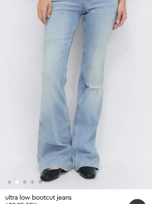 Ljusblå bootcut jeans med slitningar - Snygga ljusblå bootcut jeans med låg midja och slitna detaljer på låren och knäna. Jeansen har en klassisk femficksmodell och är perfekta för en avslappnad och trendig look. Passar dig som gillar retrovibbar och en bekväm passform.