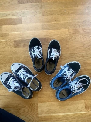 Blå och svarta Vans, svarta converse Old Skool sneakers - Säljer ett par klassiska Vans Old Skool sneakers i blått och ett par svarta i platå. Båda med vit sula och vita snören.Skorna har den ikoniska vita sidan och är tillverkade i canvas och mocka.  Samt ett par låga svarta converse. Perfekta för en avslappnad streetwear-look. Alla 3 har storlek 36,5 och säljs i ett paketpris för 450kr