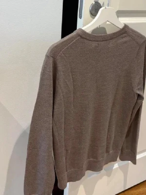 Brun stickad tröja med rund hals - En enkel och stilren brun stickad tröja med rund hals och långa ärmar. Tröjan har en rak passform och ribbade muddar vid ärmslut och nederkant. Perfekt att matcha med jeans eller kjol för en avslappnad look.