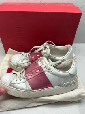Valentino open - Säljer ett par vita sneakers från Valentino med bred metallicrosa panel över snörningen och klassisk snörning framtill. Skorna har en chunky sula och är tillverkade i skinn. Perfekta för dig som vill ha en statement sneaker med lyxig känsla.