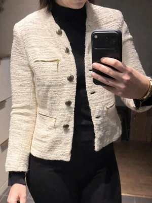 Vit kavajjacka från Zara med dragkedjor - Snygg vit kavajjacka från Zara med strukturerat tyg och silvriga knappar. Jackan har flera dekorativa dragkedjor framtill och på ärmarna, vilket ger en cool och modern vibe. Perfekt för dig som gillar stilrena detaljer och vill sticka ut.