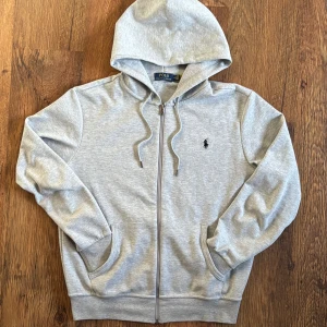 Grå zip hoodie från Polo Ralph Lauren - Snygg ljusgrå hoodie med dragkedja från Polo Ralph Lauren. DM för frågor/fler bilder. Skickar inom 24h✅📩