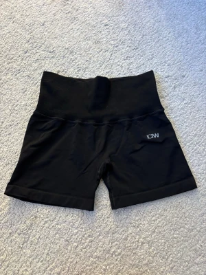 Svarta högmidjade shorts från ICIW - Säljer ett par svarta högmidjade shorts från ICIW. De har en bred ribbad midja och en praktisk dold dragkedjeficka baktill. 