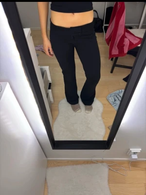 Soft flare Nelly kostymbyxor - Säljer ett par svarta kostymbyxor med utsvängda ben och låg midja. Byxorna har en stilren look med diskreta fickor och klassisk stängning fram. Materialet känns mjukt och stretchigt vilket gör dem riktigt bekväma att bära.