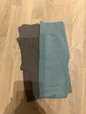 Två par leggings i grått och blått - Säljer två par leggings, ett par i ljusblått och ett par i mörkgrått. Båda har hög midja och är tillverkade i stretchigt material som sitter skönt på kroppen. Perfekta för en avslappnad och trendig look.