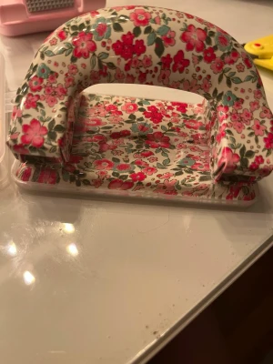 Blommig hålslagare i metall - Säljer en hålslagare i metall med färgglatt blommigt mönster i rosa, rött och grönt på vit botten. Perfekt för att piffa upp skrivbordet och organisera papper på ett snyggt sätt. Klassisk form och stabil konstruktion.