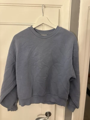 Ljusblå oversized sweatshirt - En stilren ljusblå sweatshirt i oversized modell med rund halsringning och ribbade muddar vid ärmslut och nederkant. Tillverkad i mjukt bomullsliknande material som känns skönt mot huden. Perfekt för en avslappnad och trendig look.