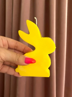 Gul kaninformad ljusdekoration - Säljer ett gult ljus i form av en kanin, perfekt som dekoration till påsk eller för att liva upp rummet. Ljusets form är tydligt kaninlik och det är tillverkat av vax. Passar dig som gillar färgglada detaljer och unika former.