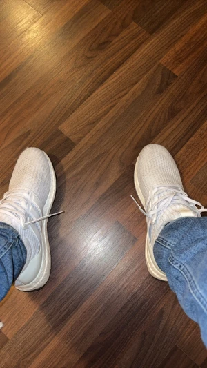 Vita Adidas Ultraboost sneakers - Säljer ett par fräscha vita Adidas Ultraboost sneakers med stickad ovandel och klassisk Boost-sula. Skorna har låga skaft och vita snören, vilket ger en clean och sportig look. Perfekta för dig som gillar stilrena och bekväma sneakers.