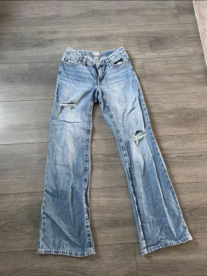Ljusblå slitna raka jeans - Säljer ett par ljusblå jeans med raka ben och slitningar på båda benen. Jeansen har klassisk femficksdesign och en avslappnad passform. Perfekta för en casual och trendig look. Materialet är denim i bomull.