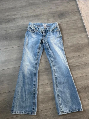Ljusblå bootcut jeans från Gina tricot - Säljer ett par ljusblå bootcut jeans från Gina tricot med klassisk femficksdesign och snygga slitningar. Jeansen har låg midja och utsvängda ben, perfekta för en avslappnad och trendig look. Materialet är mjukt denim i bomull.