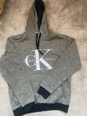 Grå hoodie från Calvin Klein Jeans - Snygg grå/grön hoodie från Calvin Klein Jeans med stor CK-logga framtill. 