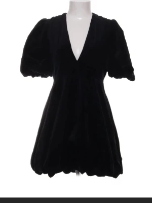 Svart kort sammet  klänning med puffärm - Stilren svart kort klänning med puffiga kortärmar och v-ringning. Klänningen har en luftig passform och ballongformad nederkant som ger en trendig siluett. Perfekt för dig som gillar en enkel men ändå statement look.