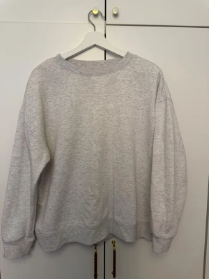 Ljusgrå sweatshirt från Primark - En basic ljusgrå sweatshirt från Primark i storlek L. Tröjan har en avslappnad passform, rund halsringning och ribbade muddar vid ärmslut och nederkant. Tillverkad i mjukt och bekvämt material, perfekt för en chill och enkel stil.