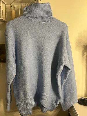 Ljusblå polotröja från BikBok - Mysig ljusblå stickad polotröja från BikBok med oversized passform och bred ribbad polokrage. Tröjan har långa ärmar och ribbade muddar vid ärmslut och nederkant. Perfekt för kalla dagar och enkel att styla till jeans eller kjol.