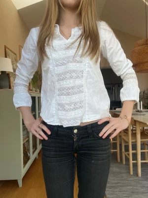 Vit blus med spetsdetaljer - Säljer en vit blus med vackra spetsdetaljer framtill och på ärmarna. Blusen har en liten v-ringning och långa ärmar. Perfekt för dig som gillar romantisk och stilren look. Materialet känns lätt och luftigt, 100% bomull.