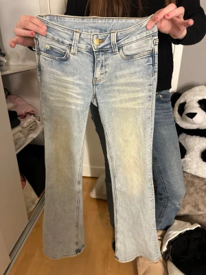 Ljusblå bootcut jeans från Cipo & Baxx - Säljer ett par ljusblå bootcut jeans från weekday med slitna detaljer och klassisk femficksmodell. Jeansen har en guldfärgad knapp, tydliga sömmar och en grön logolapp bak i midjan. Perfekta för en avslappnad och trendig look.