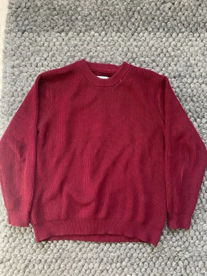 Vinröd stickad tröja Maison Margiela - Vinröd stickad tröja från Maison Margiela med klassisk rund halsringning och ribbade muddar. Tröjan har en rak passform och de ikoniska fyra vita sömmarna i nacken. Perfekt för dig som gillar minimalistisk och stilren design.