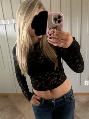 Svart spetsig croppad långärmad topp - Säljer en svart croppad topp i spets med lång ärm. Toppen är genombruten och har en tajt passform som framhäver midjan. Perfekt för dig som vill ha en edgy och trendig look. Passar snyggt till både jeans och kjol. strl L men passar mig som brukar ha S/M❤️