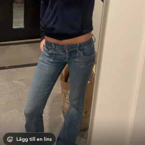 Blå bootcut jeans - Säljer ett par snygga blå bootcut jeans med låg midja. Perfekta för en avslappnad stil. De har ett litet hål vid gylfen som jag sytt ihop men annars är de i bra skick!!