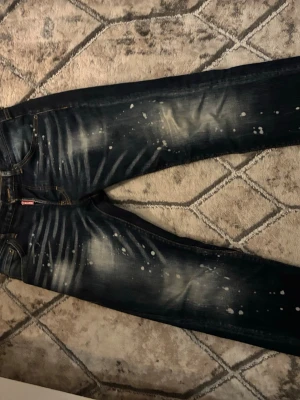 Mörkblå jeans med blekta detaljer - Säljer ett par mörkblå jeans från Diesel med coola blekta partier och vita splash-effekter. Jeansen har klassisk femficksdesign och raka ben. Materialet är slitstark denim som ger en snygg och trendig look.