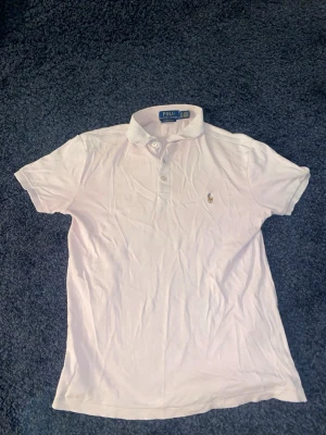 Ljusrosa piké från Ralph Lauren XS - Säljer en ljusrosa pikétröja från Polo Ralph Lauren i modellen Custom Slim Fit. Klassisk krage, korta ärmar och knappar framtill. Ikoniska broderade loggan på bröstet. Perfekt för en clean och stilren look.