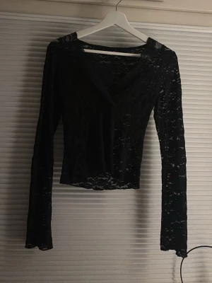 Svart spetsblus från Gina Tricot - Säljer en svart långärmad spetsblus från Gina Tricot i storlek XS. Blusen har v-ringning och är helt i genombruten spets med blommigt mönster. Perfekt att styla med ett linne under för en trendig look.