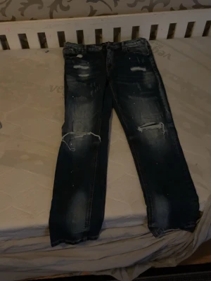 Mörkblå slitna jeans Supply & Demand - Säljer ett par mörkblå jeans från Supply & Demand med slitningar och hål på knäna. Jeansen har en tvättad look och raka ben. Perfekta för dig som gillar en avslappnad och trendig stil.