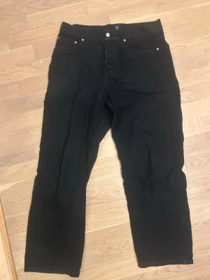 Svarta raka manchesterbyxor - Säljer ett par svarta manchesterbyxor med rak passform och klassisk femficksdesign. Byxorna har synliga silverfärgade nitar och knappar samt breda manchesterränder för en retrovibe. Perfekta för dig som gillar en avslappnad men ändå stilren look.