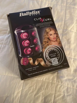 BaByliss Clip & Curl värmespolar - BaByliss Clip & Curl värmespolar med auto-clip system för enkla lockar. Innehåller spolar i två storlekar, 17 mm och 22 mm, i svart och rosa plast. Perfekt för att skapa naturliga lockar snabbt och smidigt.
