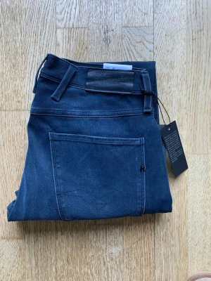 Mörkblå jeans Replay anbass  - Snygga mörkblå skinny jeans från Replay med klassisk femficksdesign och diskret logga på bakfickan. Jeansen har stretchigt material och smal passform som sitter tajt längs benen. Perfekta för en trendig och stilren look.