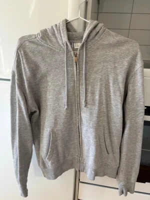 Grå zip hoodie från H&M - Säljer en gråmelerad hoodie från H&M med dragkedja framtill, två fickor och justerbar huva med snören. Storlek XS, fint skick. 