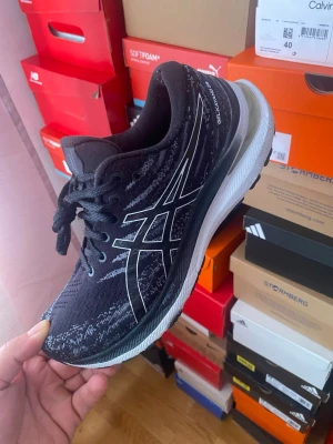 Svarta Asics sneakers med vit sula - Snygga svarta Asics sneakers med vit och grå sula. Skorna har en stickad ovandel med grå detaljer och den klassiska Asics-loggan i vitt på sidan. Lågt skaft och snörning framtill. Perfekta för dig som gillar sportig stil och komfort.