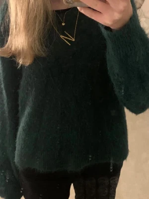 Mörkgrön fluffig stickad tröja - Mysig mörkgrön stickad tröja med fluffig yta och avslappnad passform. Tröjan har långa ärmar och rund halsringning. Perfekt för kalla dagar när du vill vara både varm och snygg.