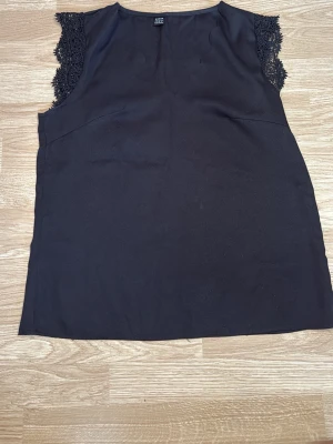 Svart ärmlös topp med spetsdetaljer - Svart ärmlös topp från Shein med spetsdetaljer vid axlarna. Toppen har en rak passform och är tillverkad i ett mjukt tyg. I storlek S.