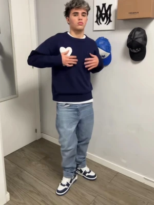 Mörkblå stickad tröja från Ami Paris - Mörkblå stickad tröja från Ami Paris med vitt hjärta och A-logga på bröstet. Tröjan har rund halsringning, ribbstickade muddar och avslappnad passform. Perfekt för en trendig och stilren look.